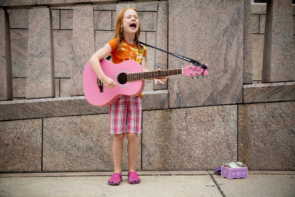 Jente med rosa gitar som synger på gata